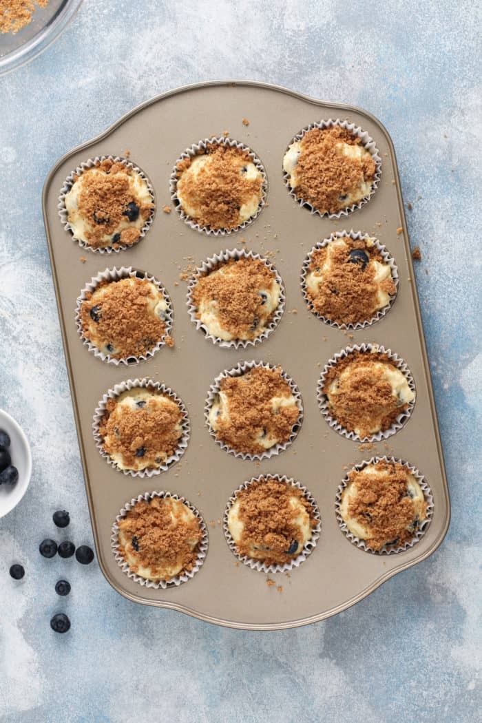 Unbaked blueberry crumb muffins in a muffin tin, ready to go in the oven.