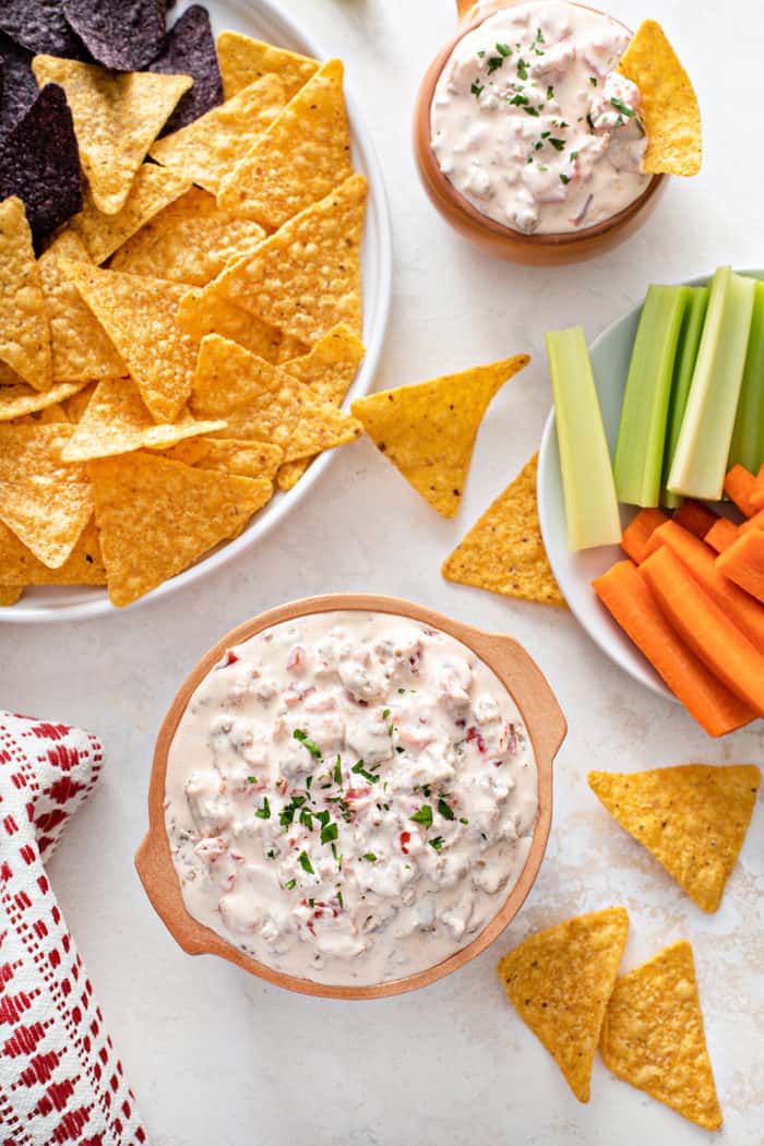 Overhead view of two bowls of spicy sausage dip surrounded by tortilla chips and fresh veggies