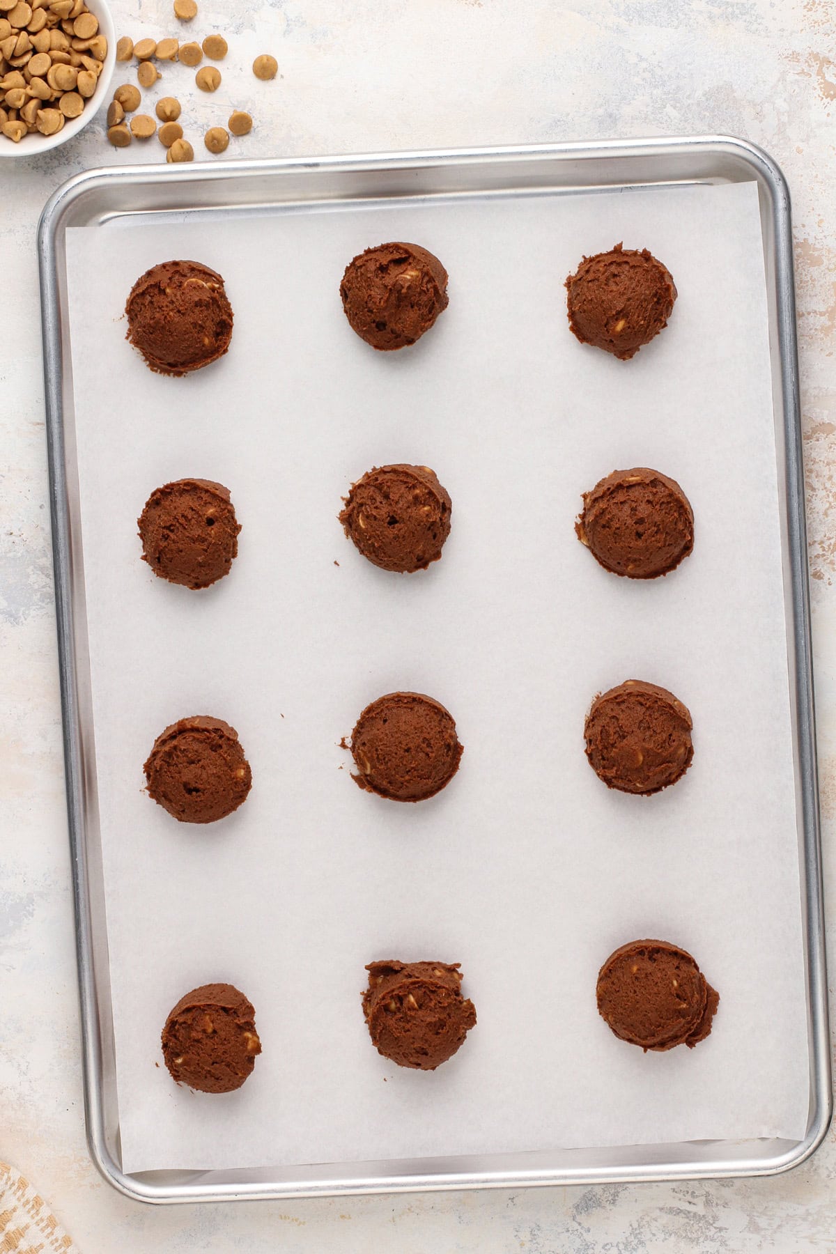 Scoops of chocolate peanut butter cookie dough on a parchment-lined baking sheet.