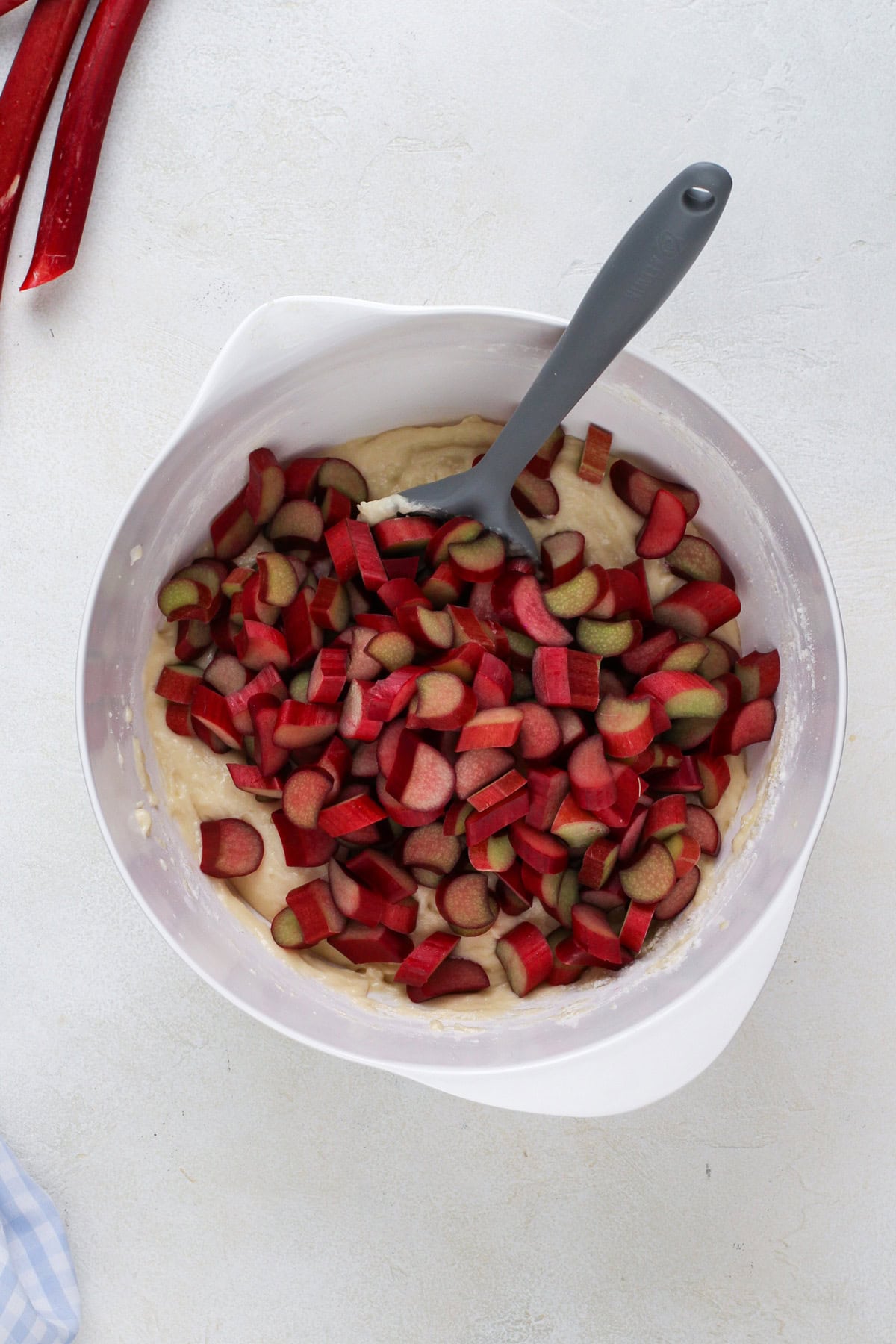 Sliced rhubarb added to a white bowl with cake batter.