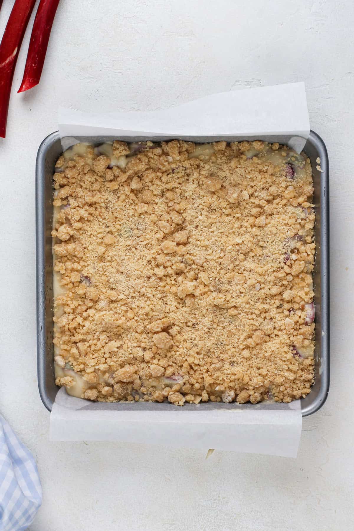 Unbaked rhubarb streusel cake in a cake pan, ready to go in the oven.