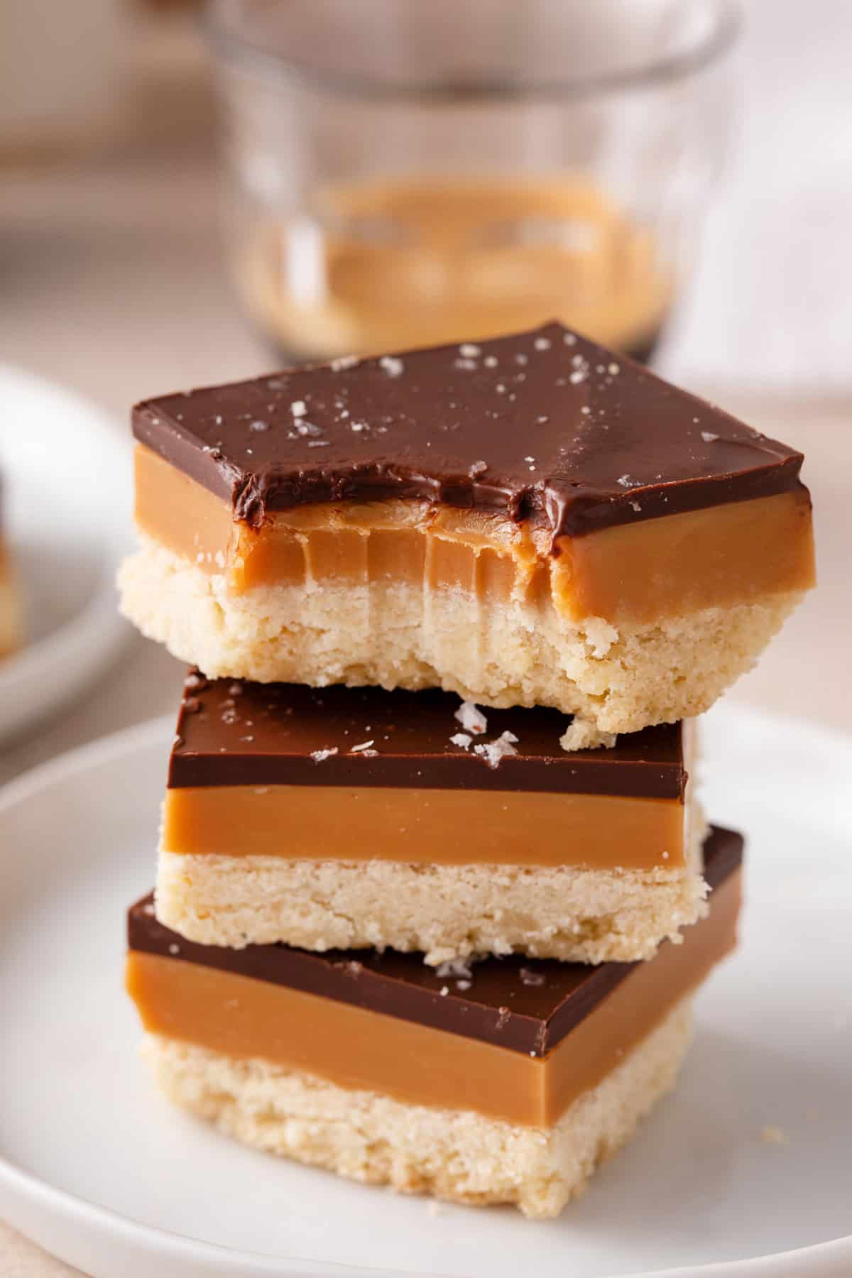 Three pieces of millionaire shortbread stacked on a plate with a bite taken from the corner.