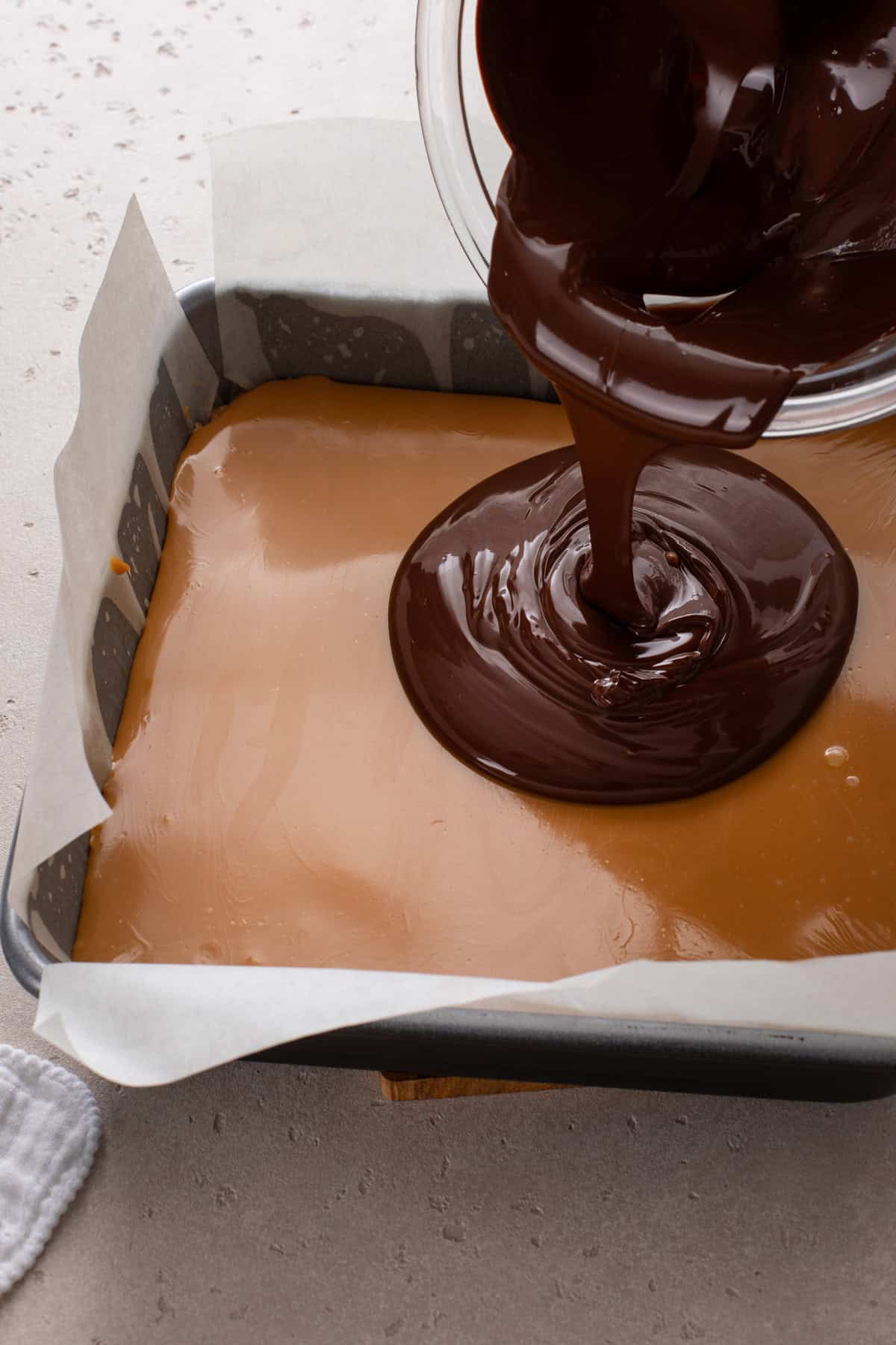 Melted chocolate being poured over the caramel layer for millionaire shortbread.