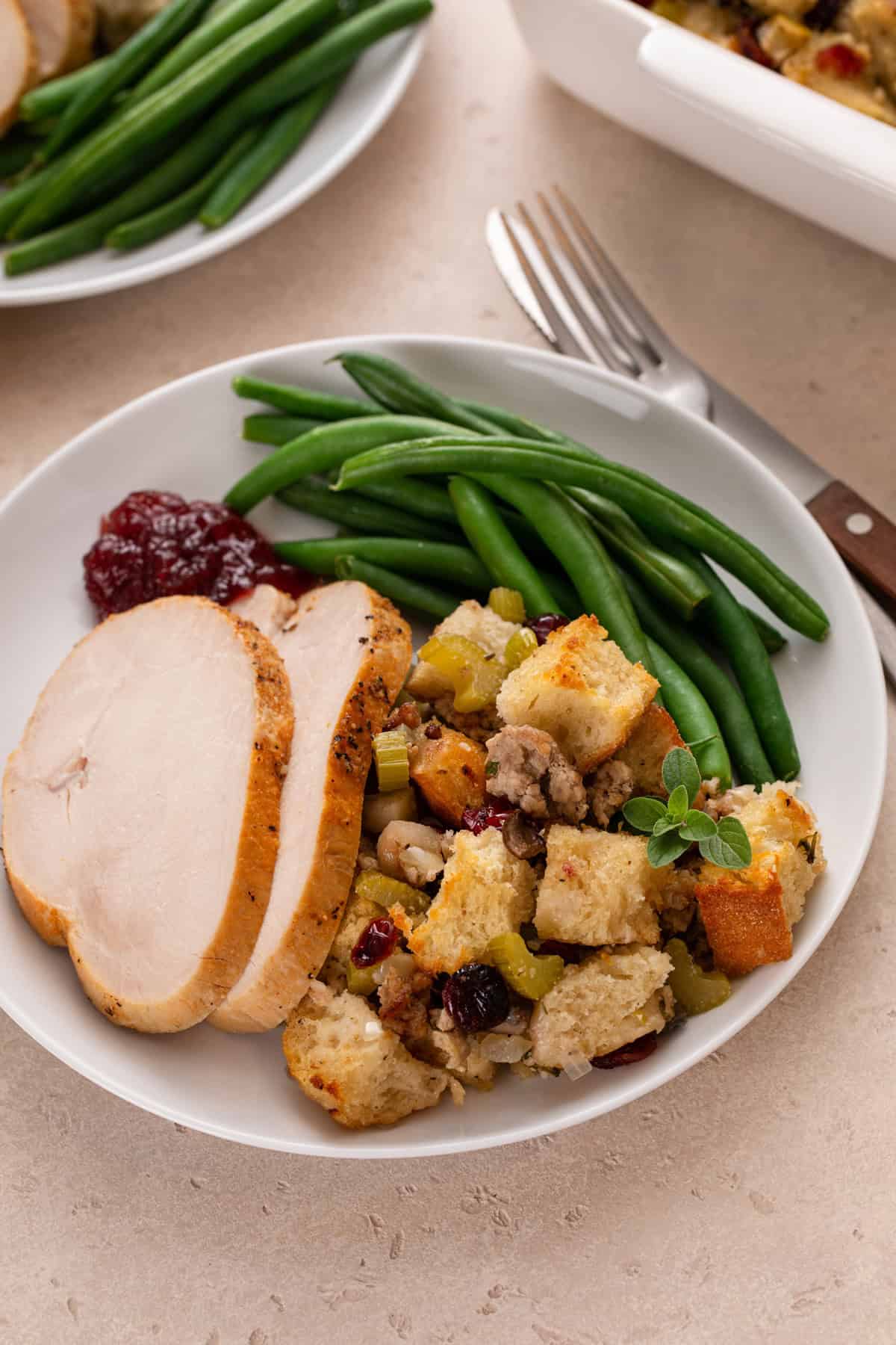 Serving of sausage and cranberry stuffing on a plate with turkey, green beans, and cranberry sauce.