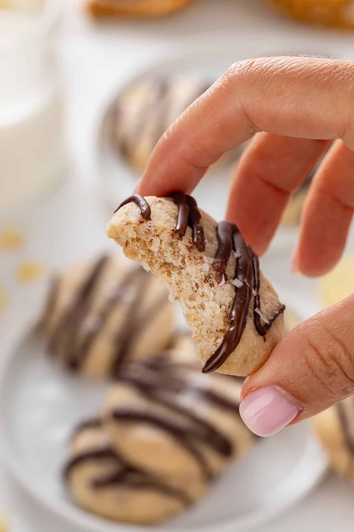 Hand holding up a chocolate-drizzled potato chip cookie with a bite taken from it.