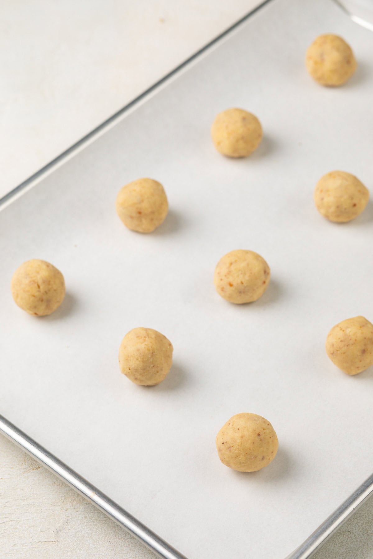 Balls of potato chip cookie dough arranged on a parchment-lined baking sheet.