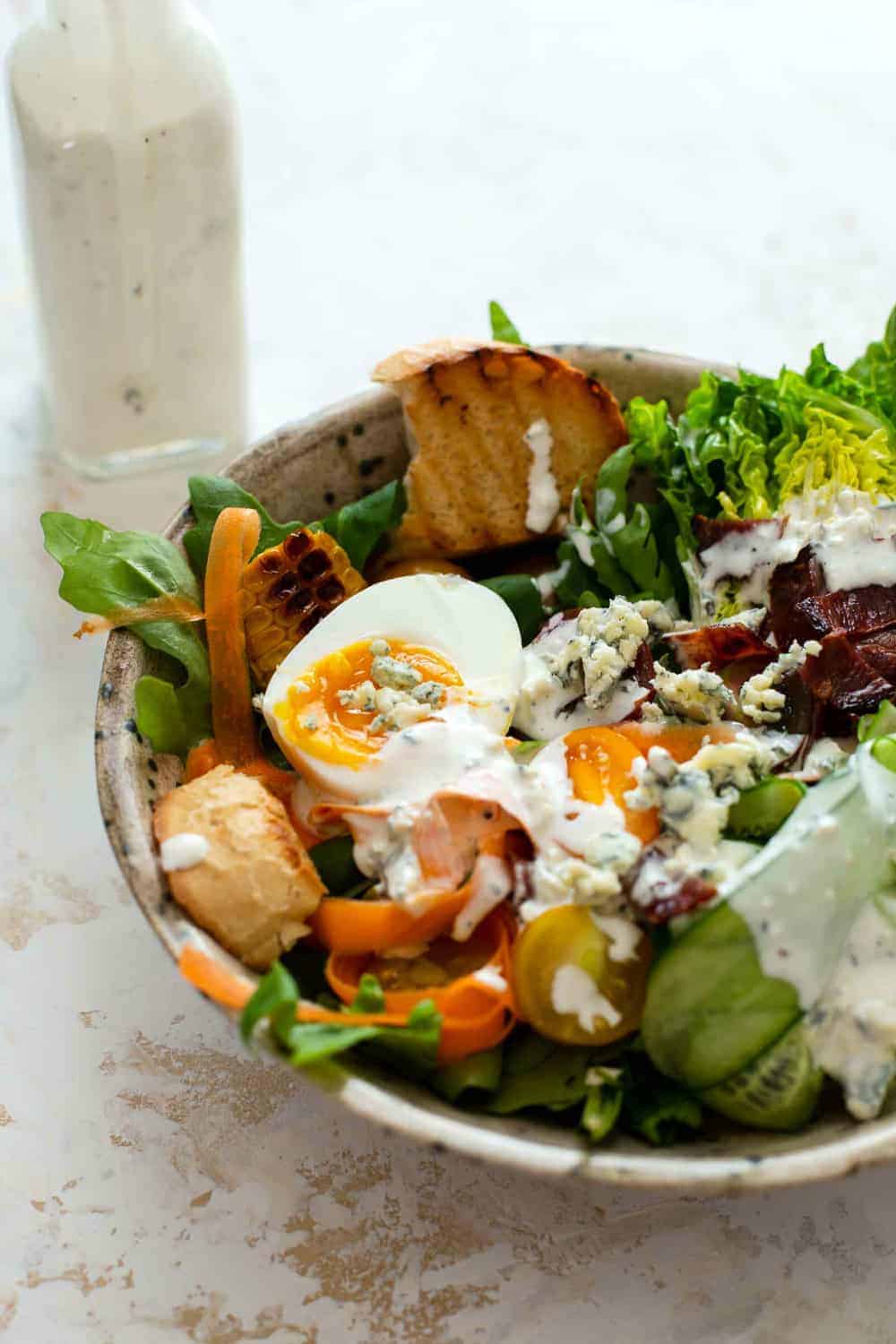 Summer salad dressed with homemade blue cheese dressing next to a bottle of blue cheese dressing