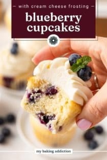 Hand holding up a blueberry cupcake with a bite taken from it. Text overlay includes recipe name.