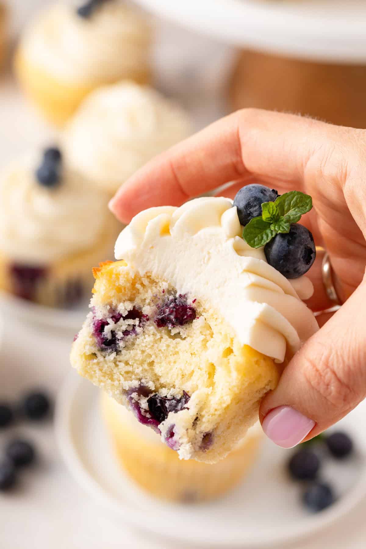 Hand holding up a blueberry cupcake with a bite taken from it.