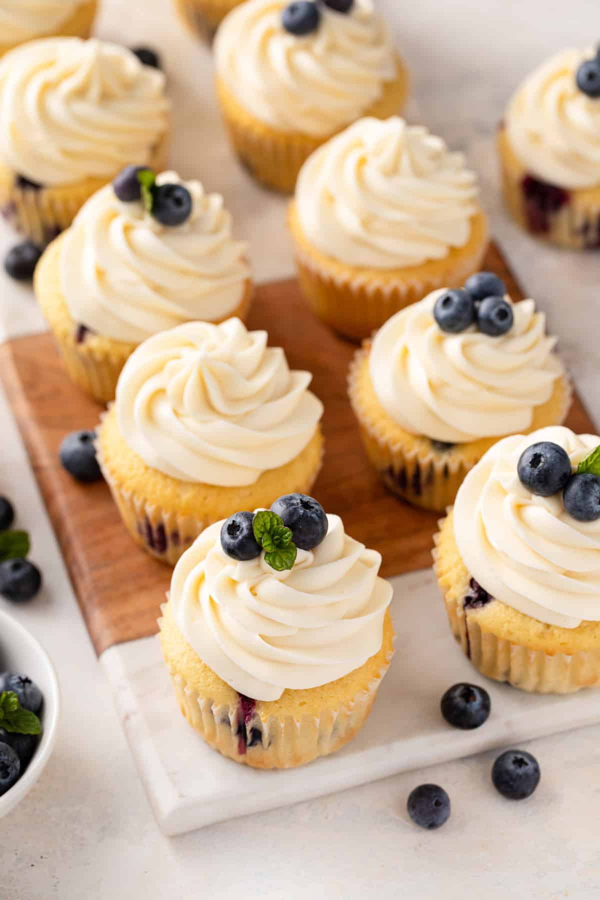 Blueberry cupcakes topped with cream cheese frosting lined up on a wood and marble board.