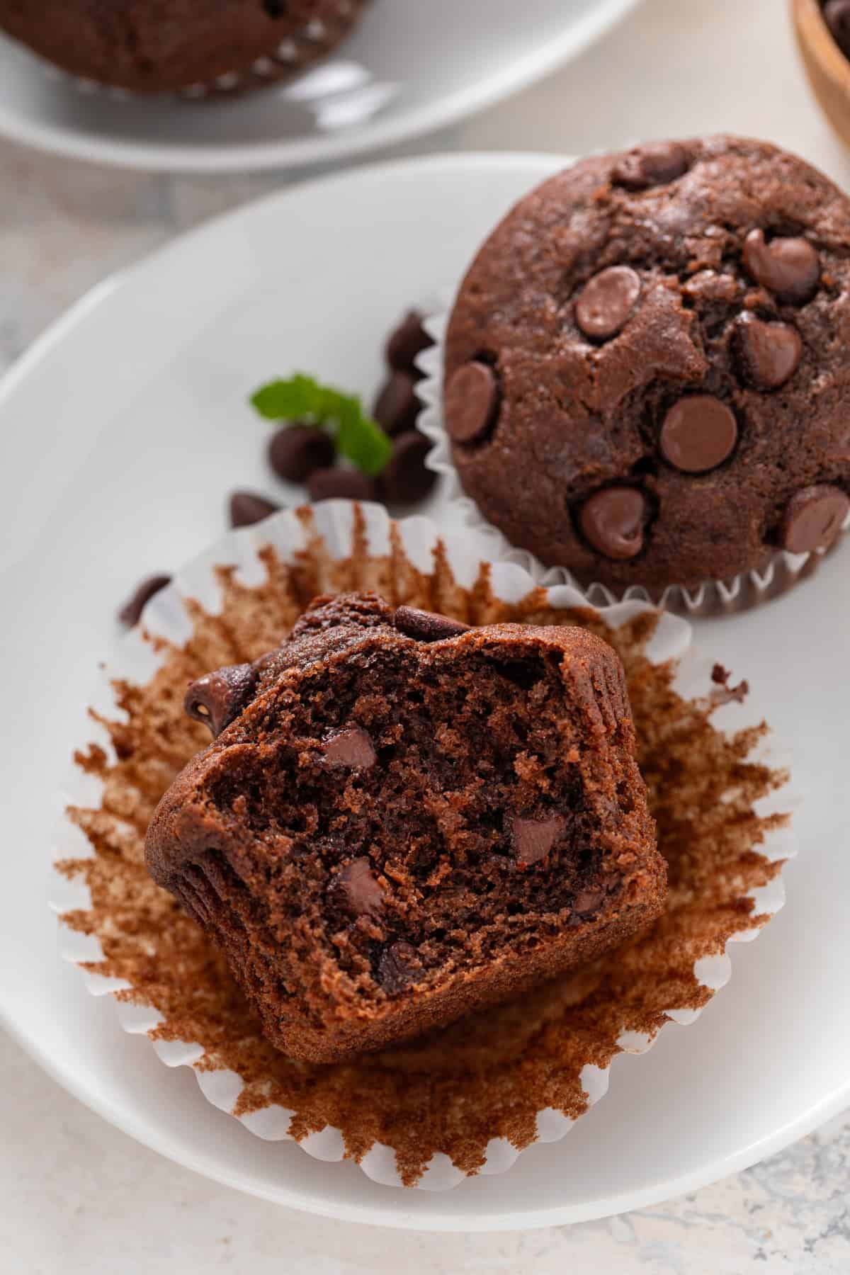 Bite taken from an unwrapped chocolate muffin on a white plate.