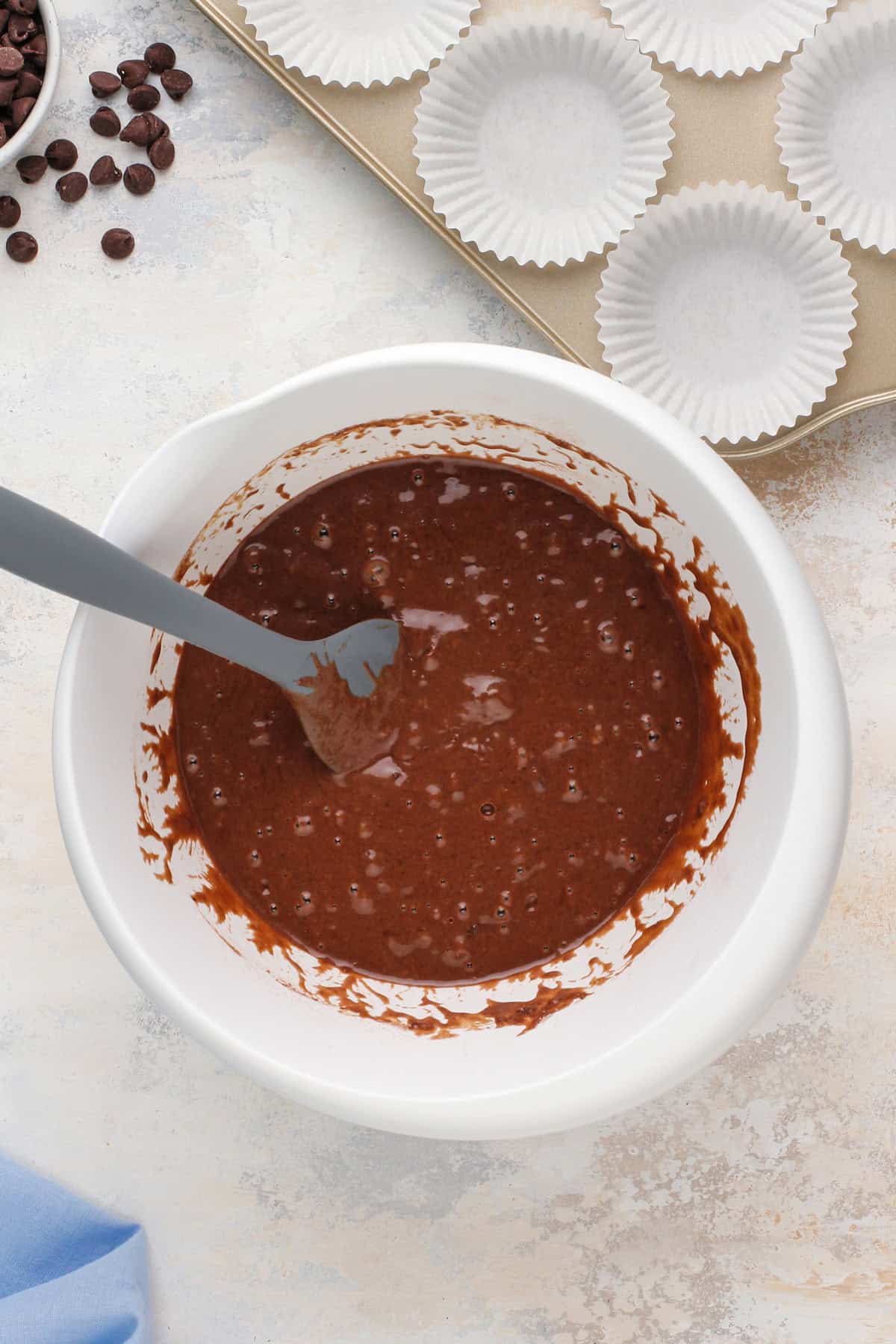 Spatula stirring double chocolate muffin batter in a white bowl.