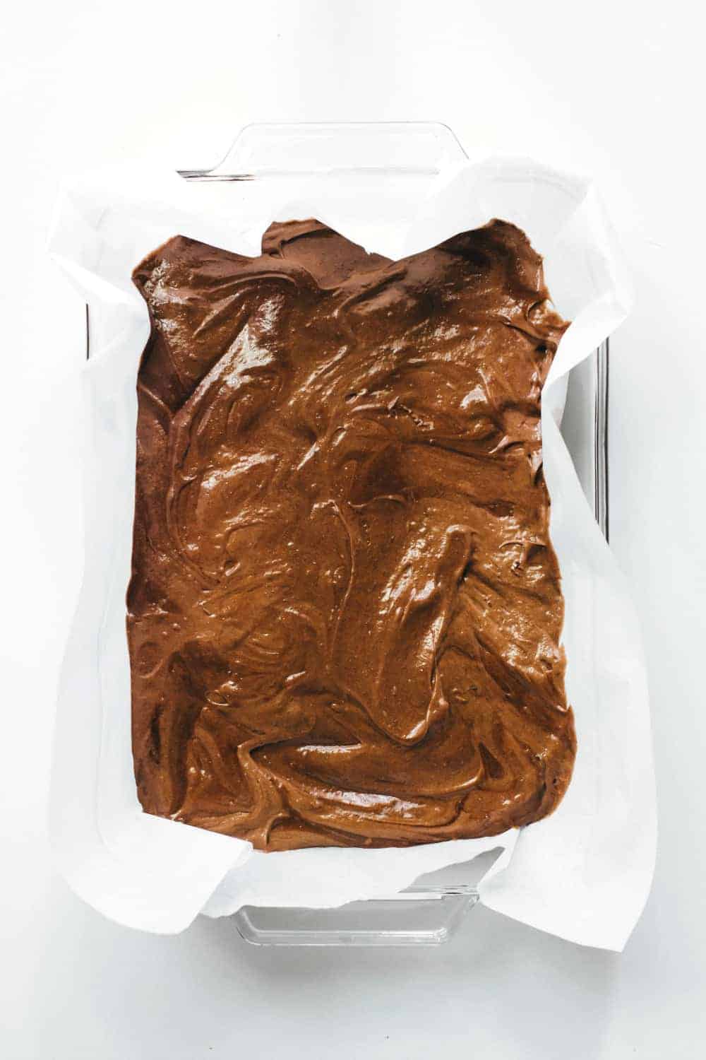 Brownie batter in a parchment-lined pan on a white surface