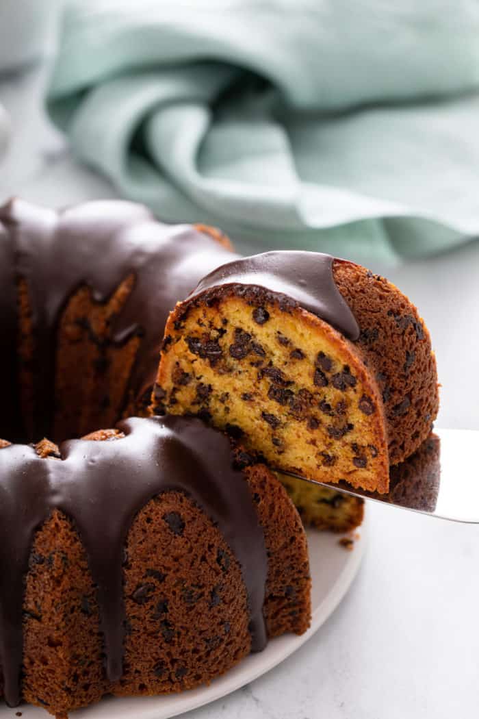 Cake server lifting up a slice of chocolate chip bundt cake from the whole cake.