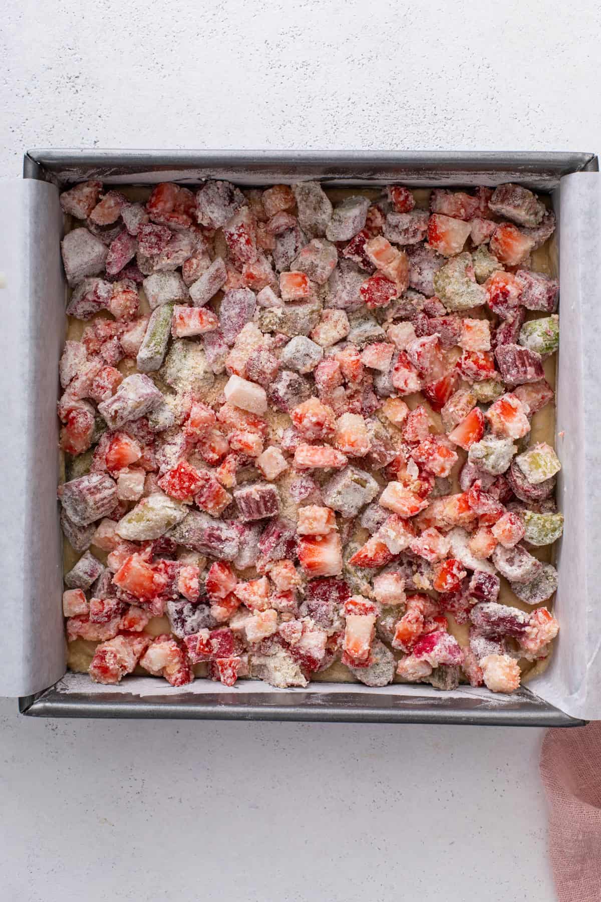 Cake batter spread in a square pan and topped with strawberry rhubarb mixture.
