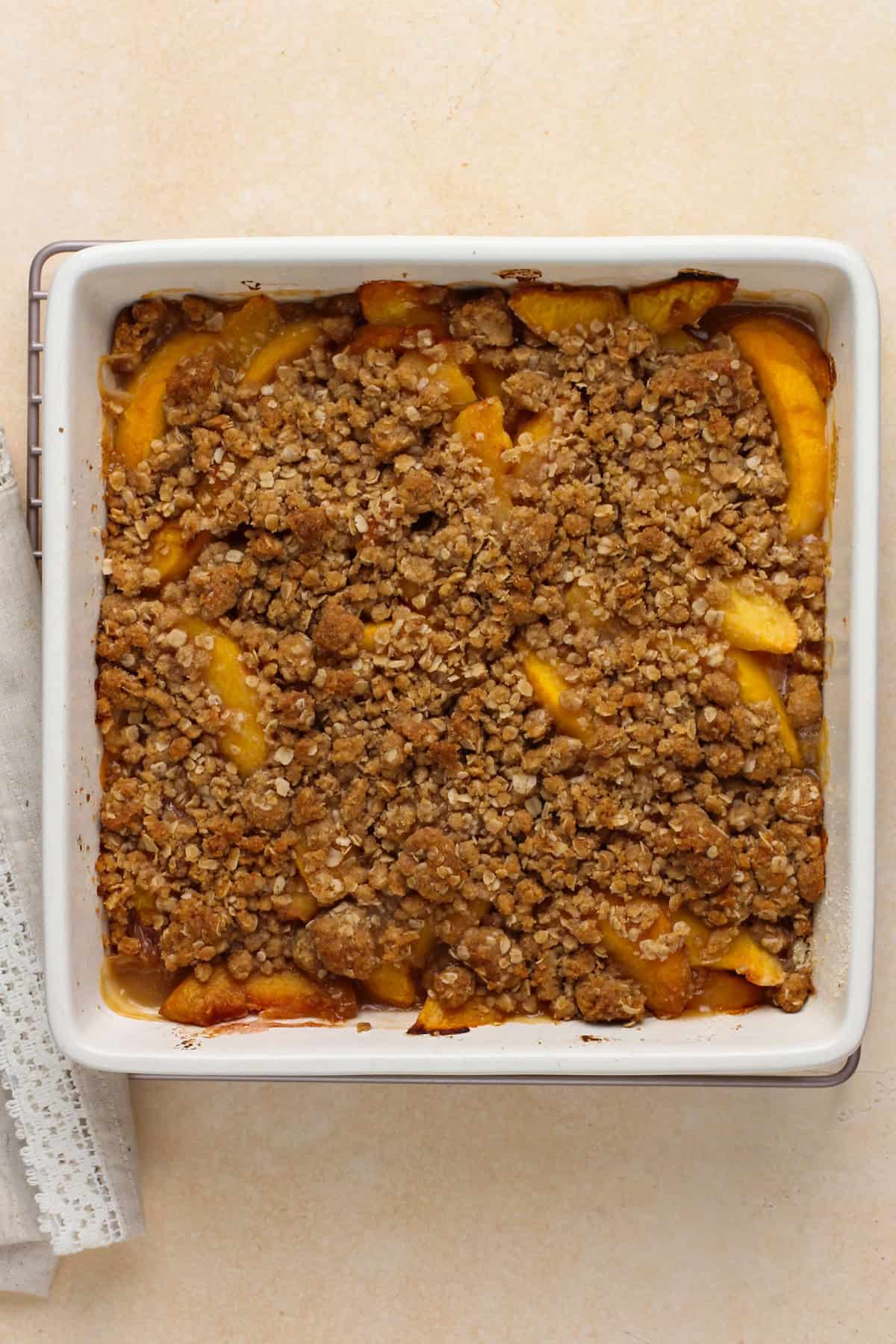 Baked peach crisp cooling in a white baking dish.