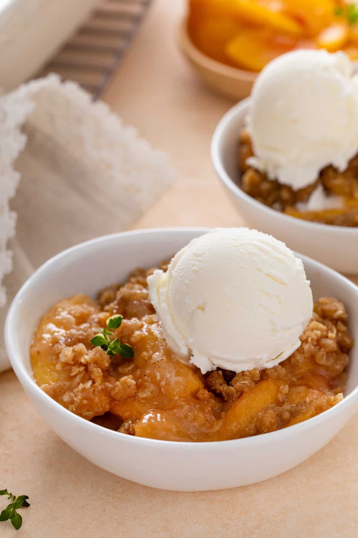 Close up of peach crisp topped with a scoop of vanilla ice cream in a white bowl.