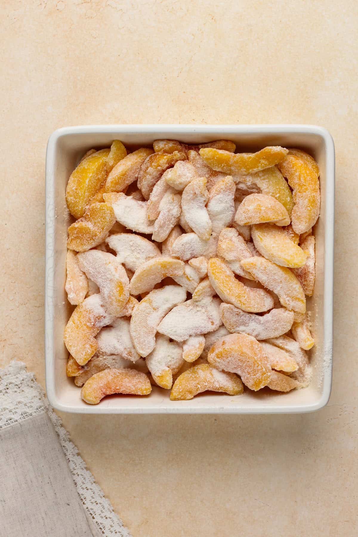 Peach crisp filling in a white baking dish.