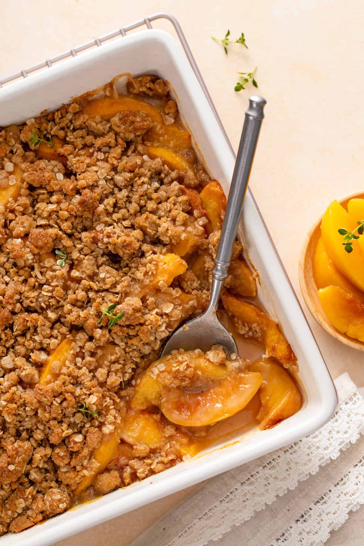 Overhead view of a spoon in the corner of a white baking dish of peach crisp.