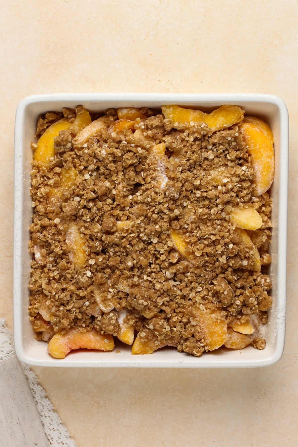 Unbaked peach crisp in a white baking dish.