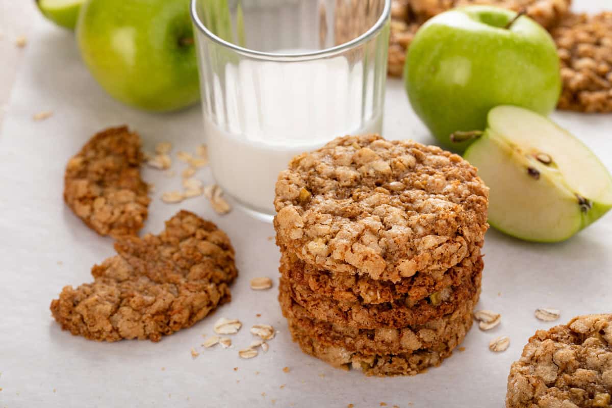 Halved apple spice cookie on a countertop next to a stack of cookies and a glass of milk.
