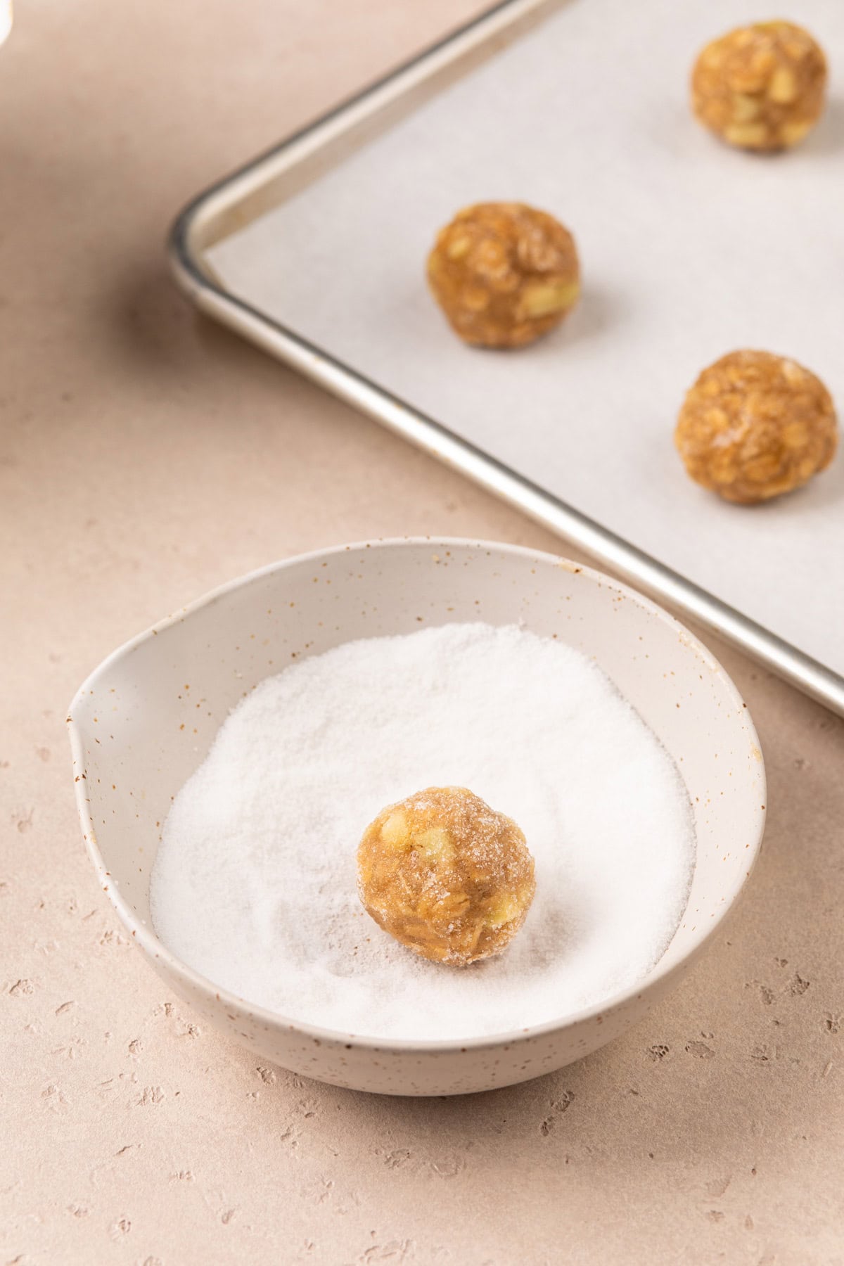Ball of apple spice cookie dough being rolled in granulated sugar.