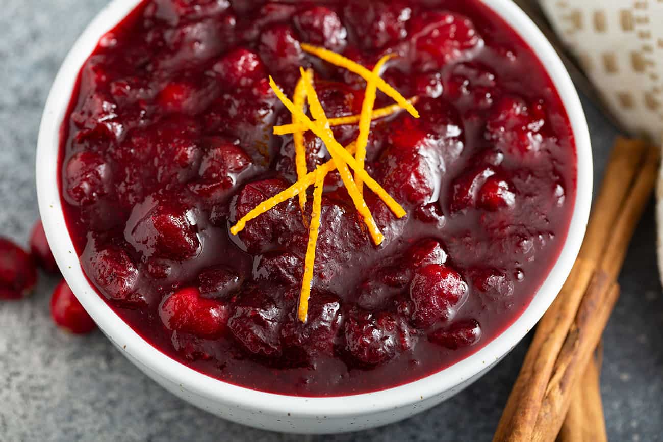 Close up of cranberry sauce in a white bowl, garnished with orange zest