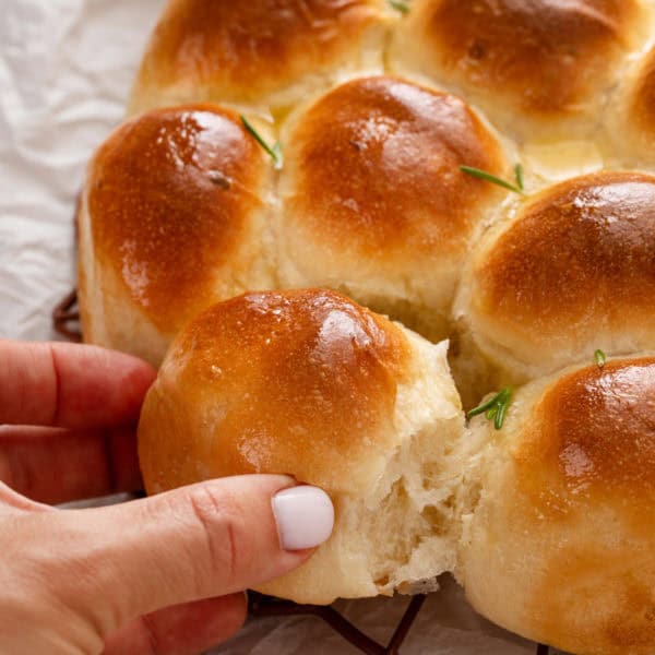 Hand pulling a brown and serve dinner roll apart from the rest of the rolls.