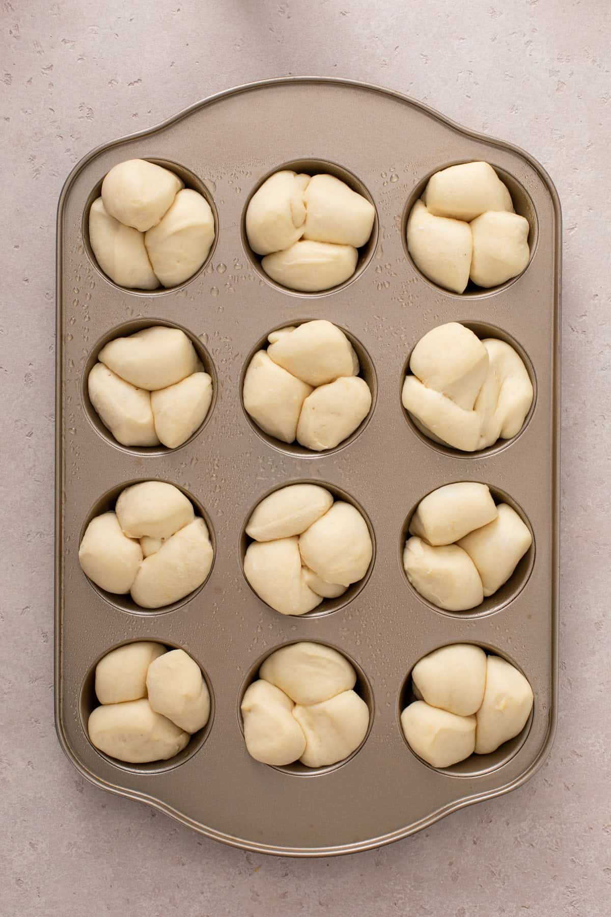 Risen cloverleaf rolls in a muffin tin, ready to bake.