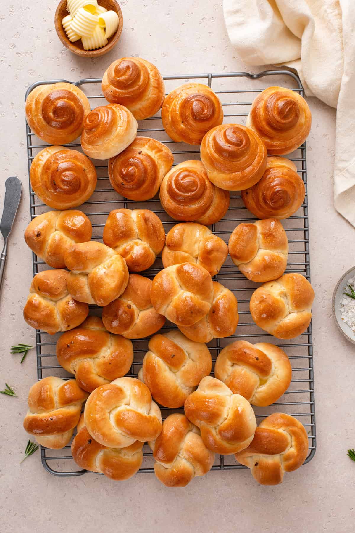 Three shapes of brown and serve dinner rolls arranged on a wire rack.