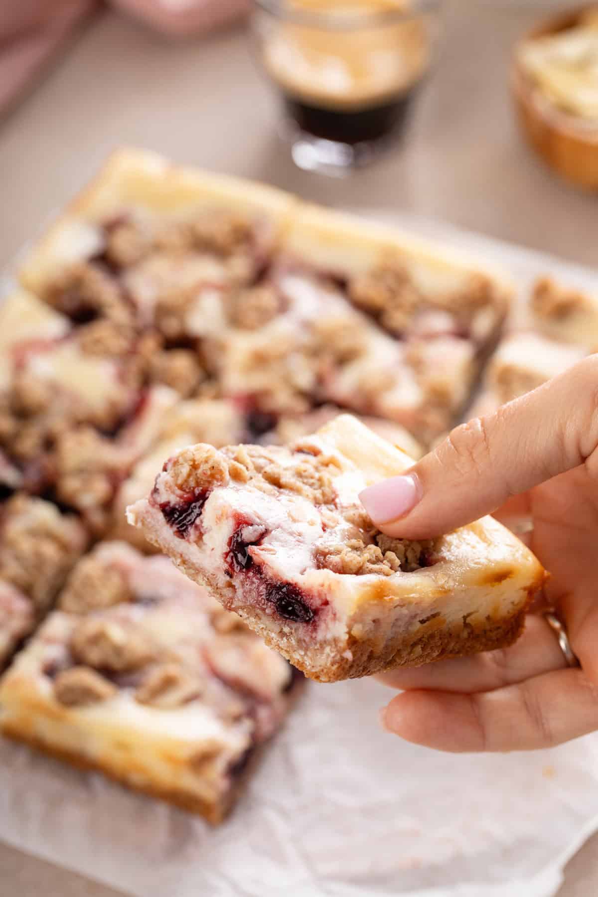 Hand holding up a cherry cheesecake bar.