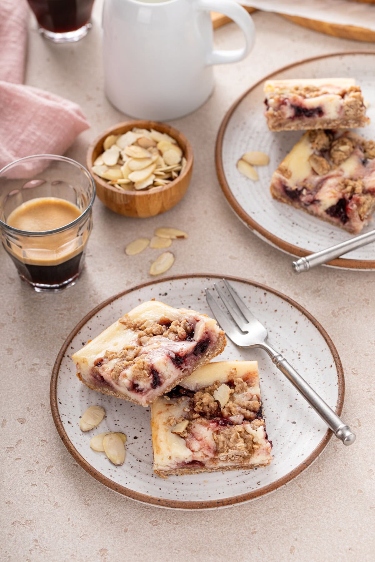 Two plates holding sliced cherry cheesecake bars and forks next to a cup of espresso.