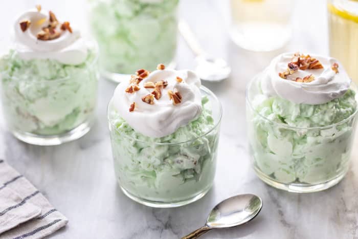 Watergate salad in four small serving dishes, topped with whipped cream and chopped pecans