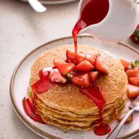 Syrup being poured over a stack of gluten-free pancakes on a white plate.