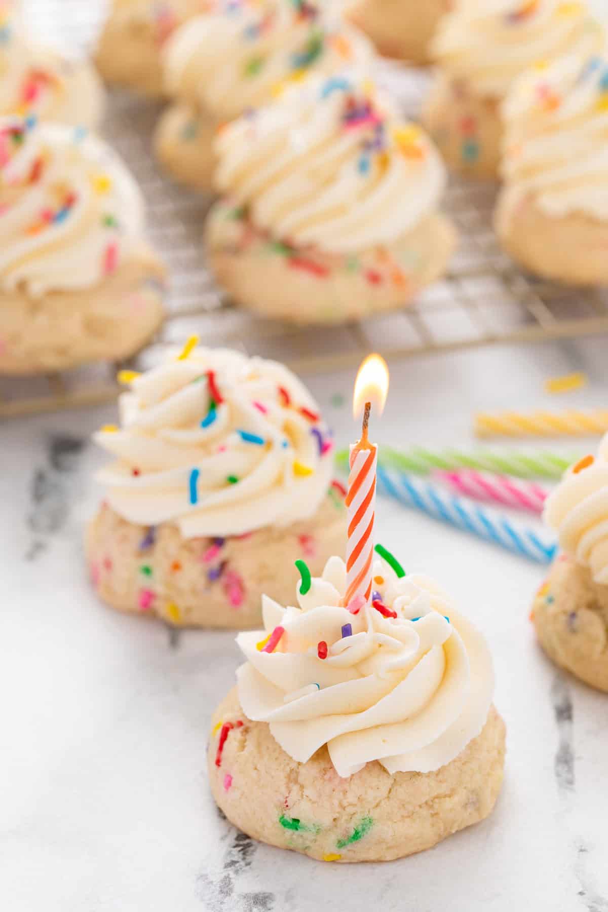 Lit birthday candle in a birthday cake cookie with more cookies in the background.