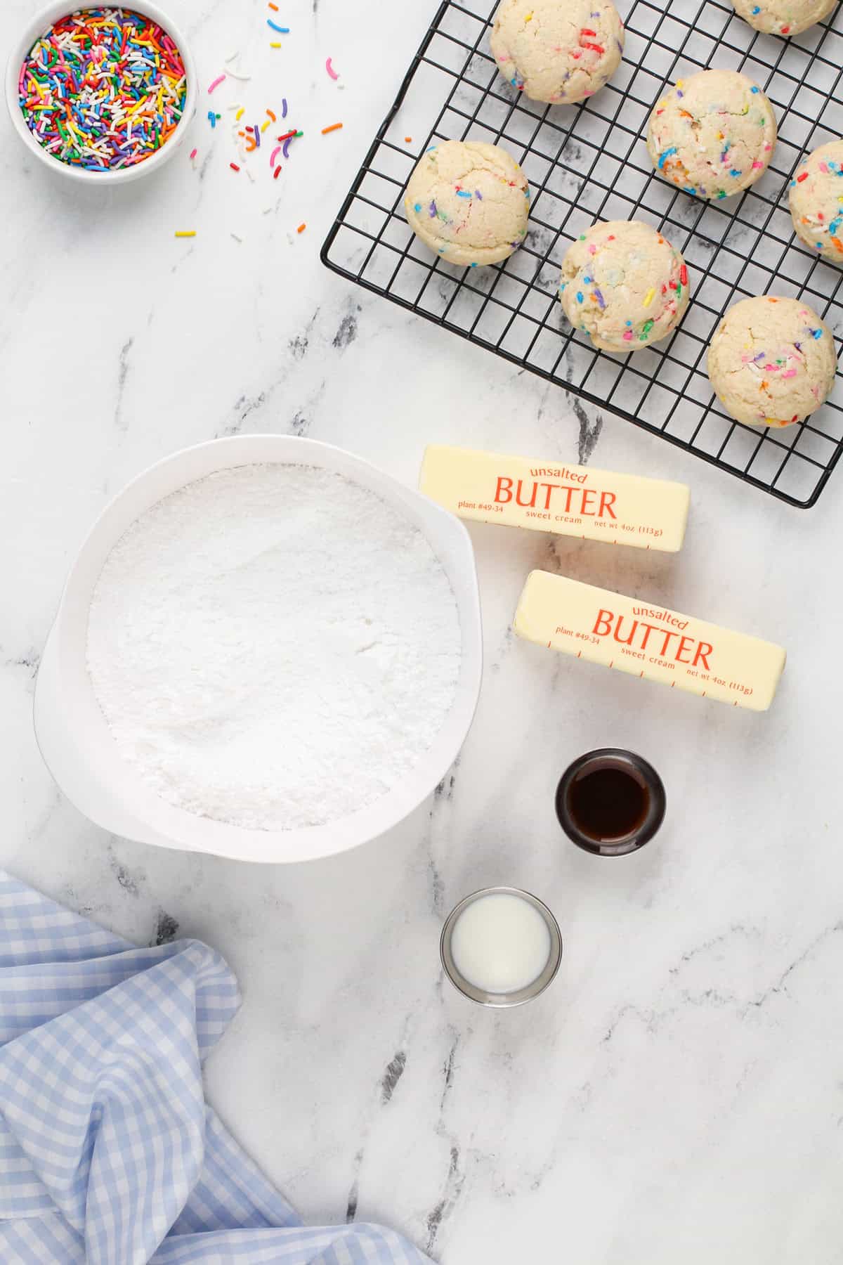 Ingredients for buttercream frosting next to baked birthday cake cookies.