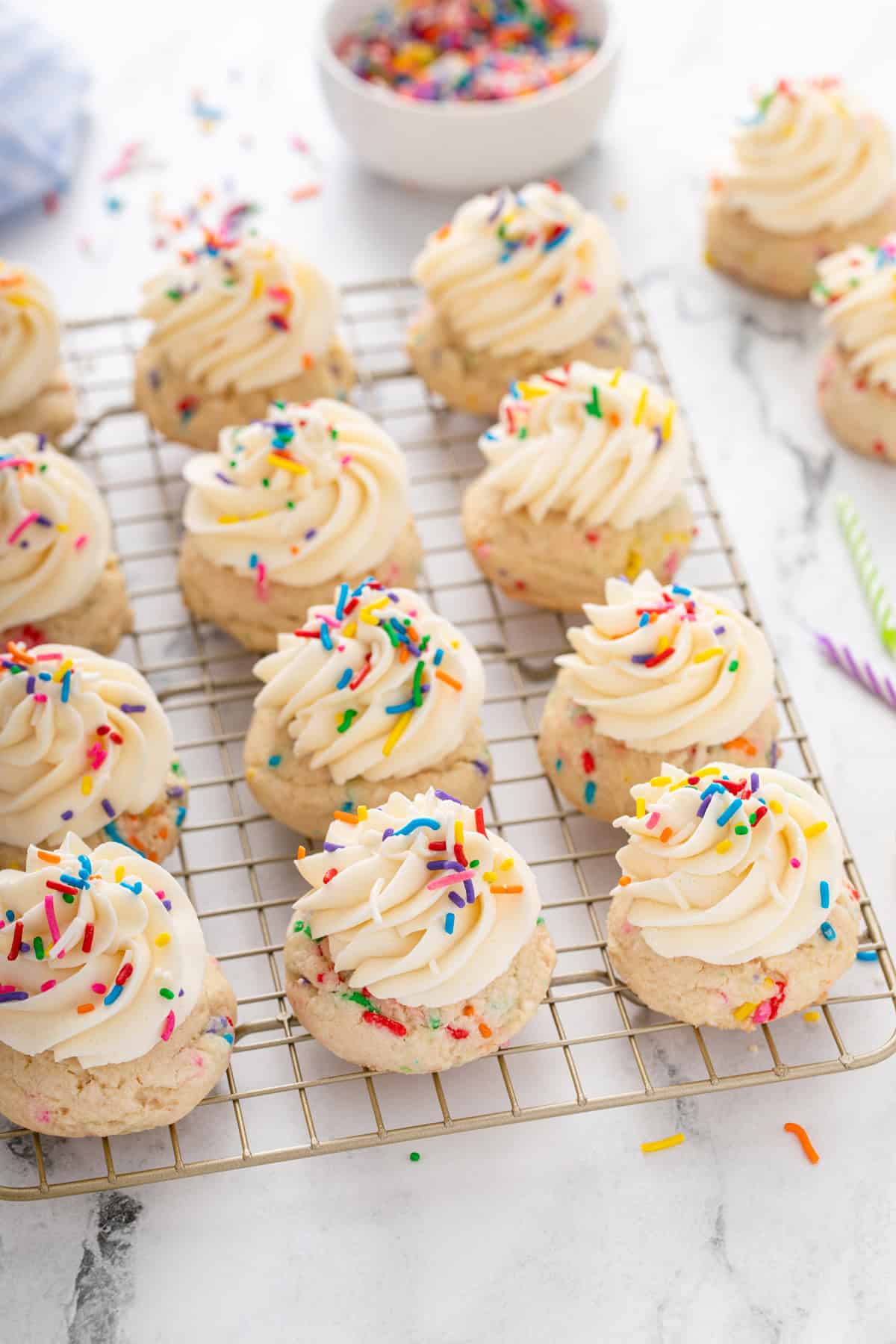 Frosted and decorated birthday cake cookies arranged on a wire rack on a marble countertop.