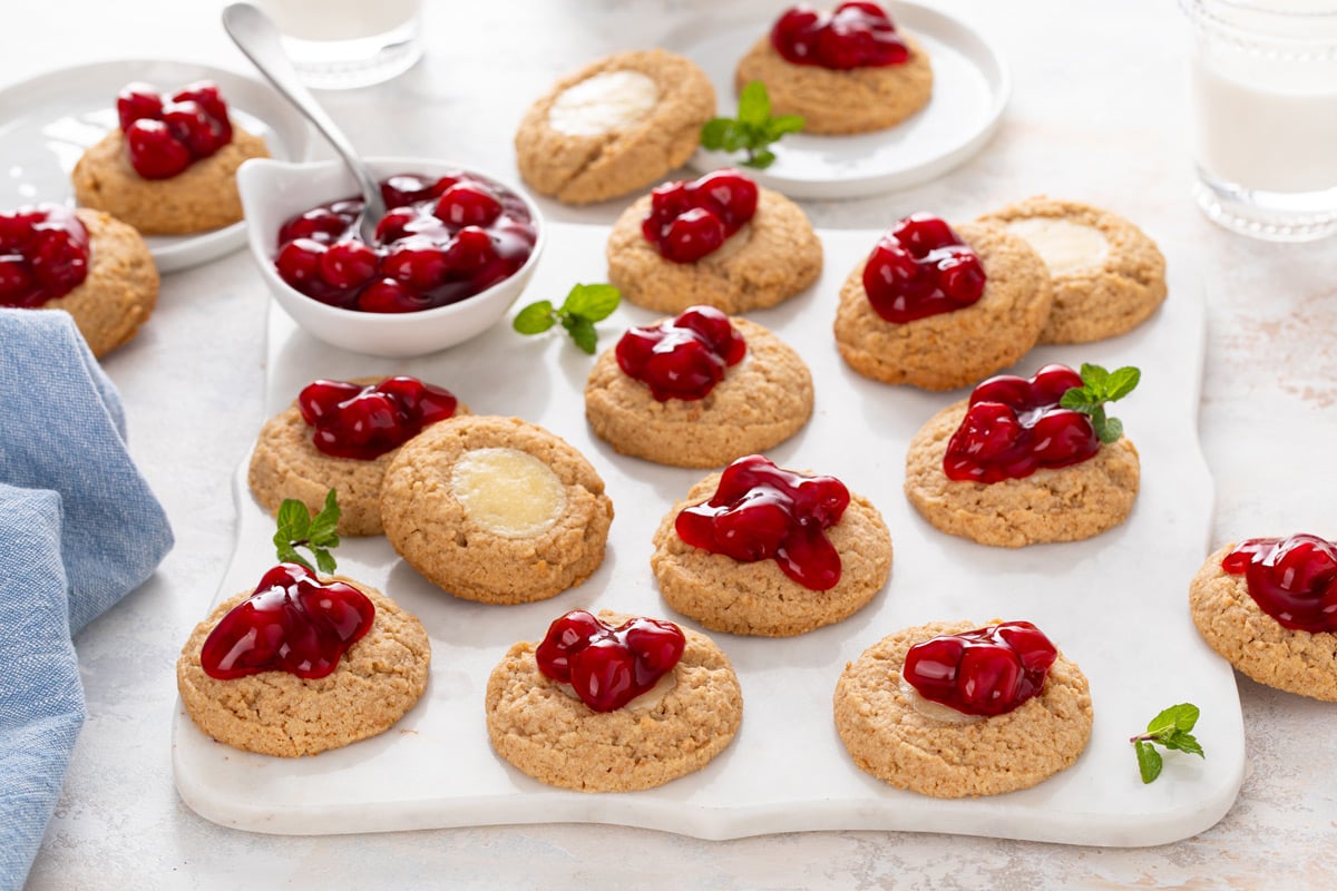 Cherry cheesecake cookies and a bowl of cherry pie filling arranged on a marble board.