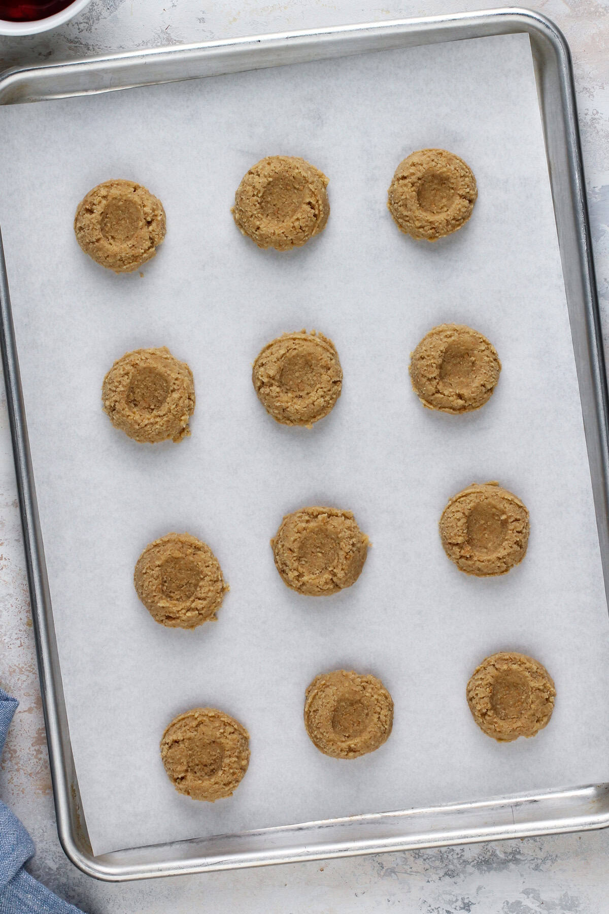 Graham cracker cookie dough arranged on a lined baking sheet with indents in each dough ball.