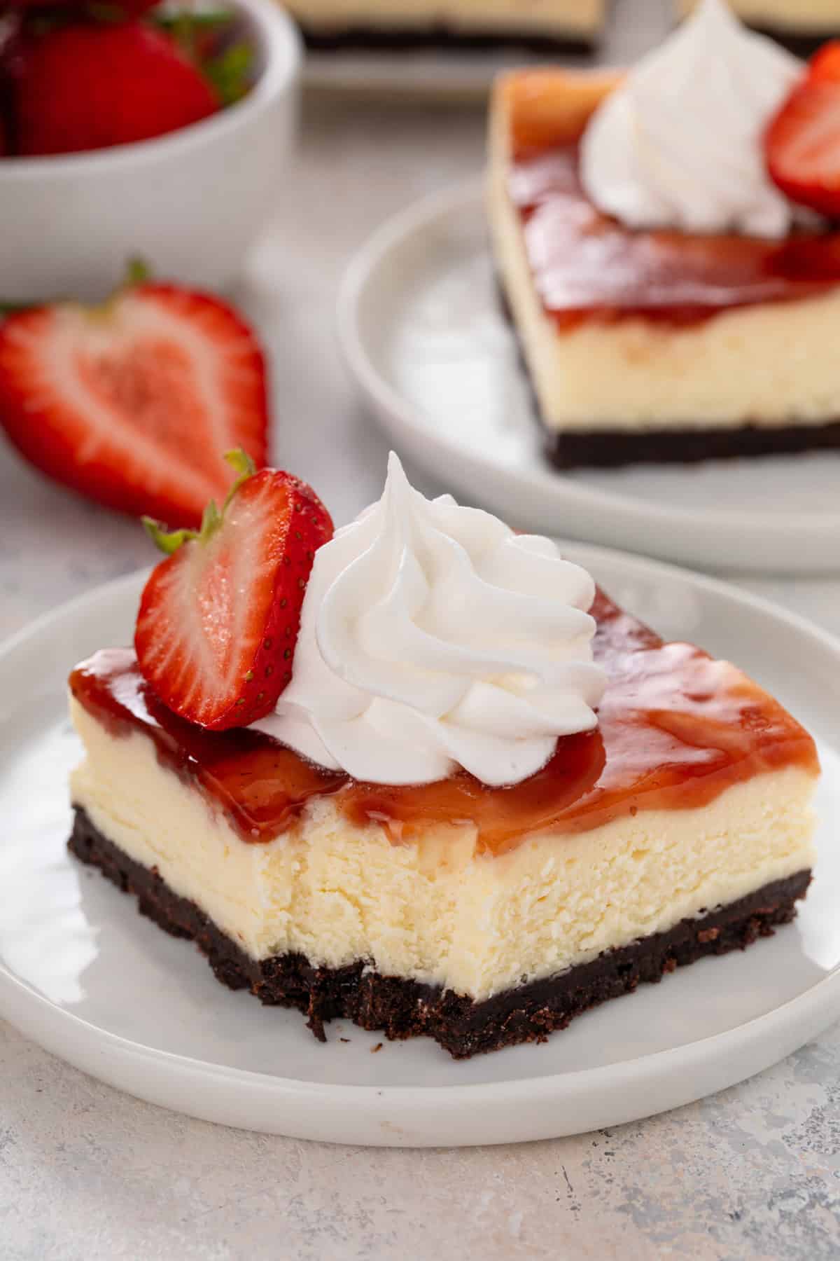 Bite taken from a plated strawberry cheesecake bar topped with whipped cream and a fresh strawberry.
