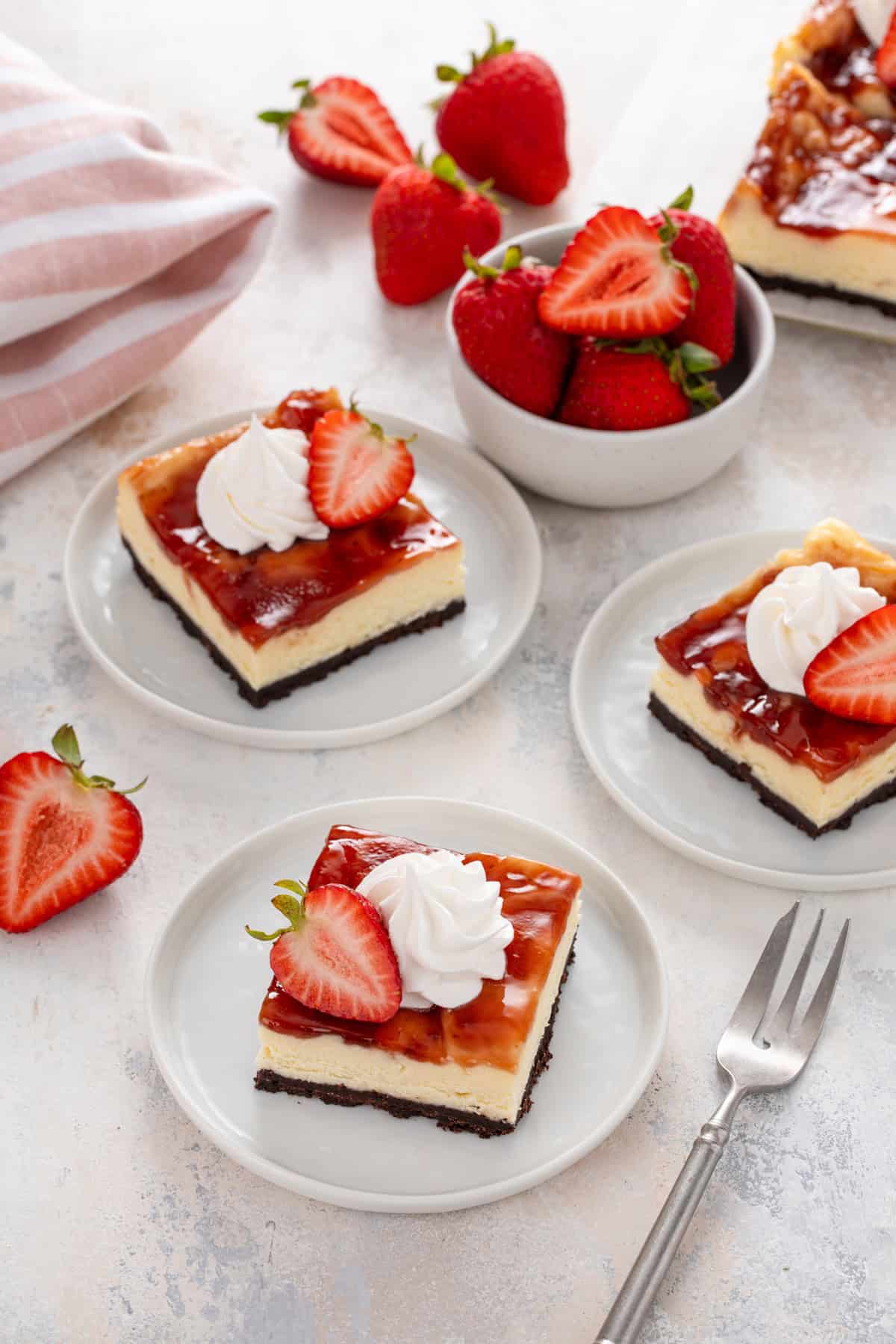 Three white plates, each holding a sliced strawberry cheesecake bar.