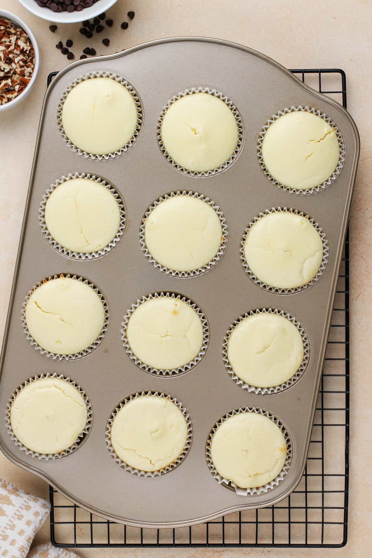 Baked mini cheesecakes in a muffin tin, cooling on a wire rack.