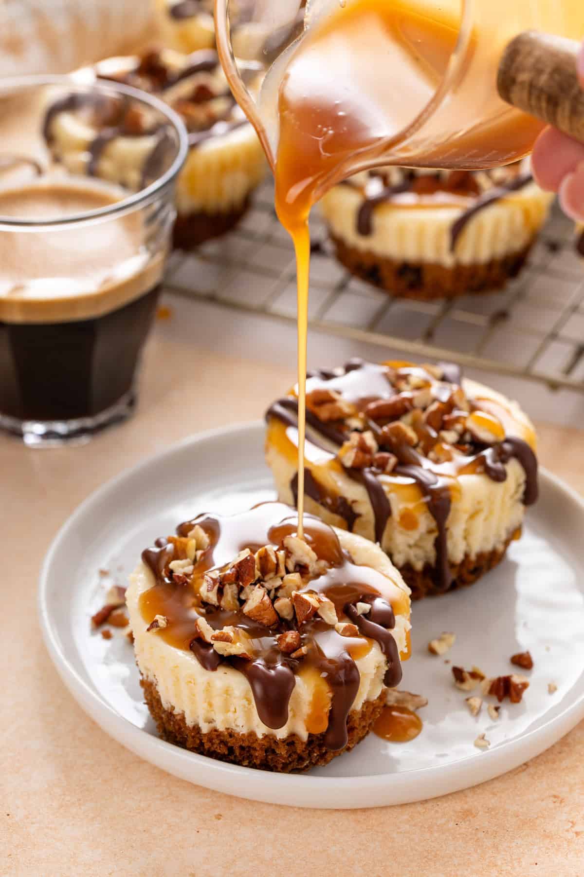 Caramel sauce being drizzled over mini turtle cheesecakes on a white plate.