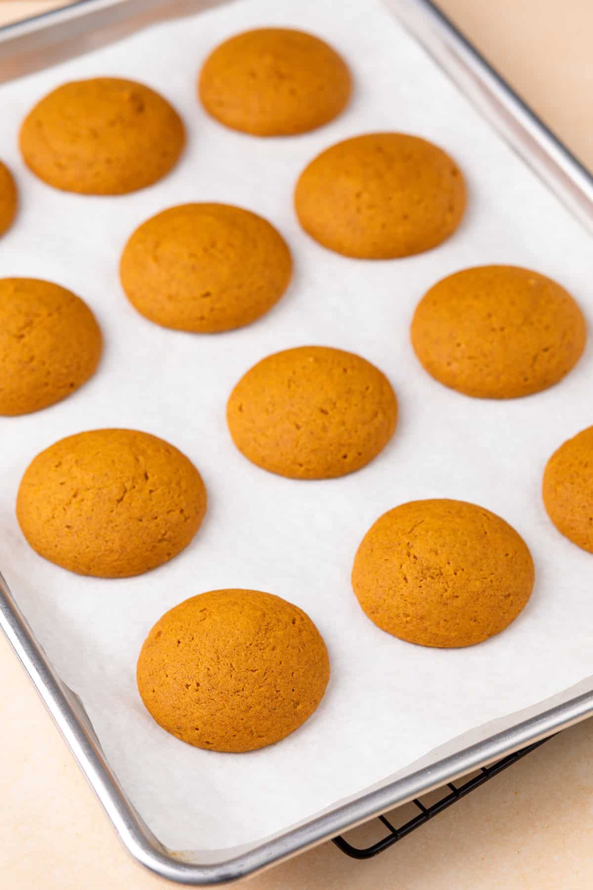 Baked pumpkin cookies for whoopie pies cooling on a baking sheet.