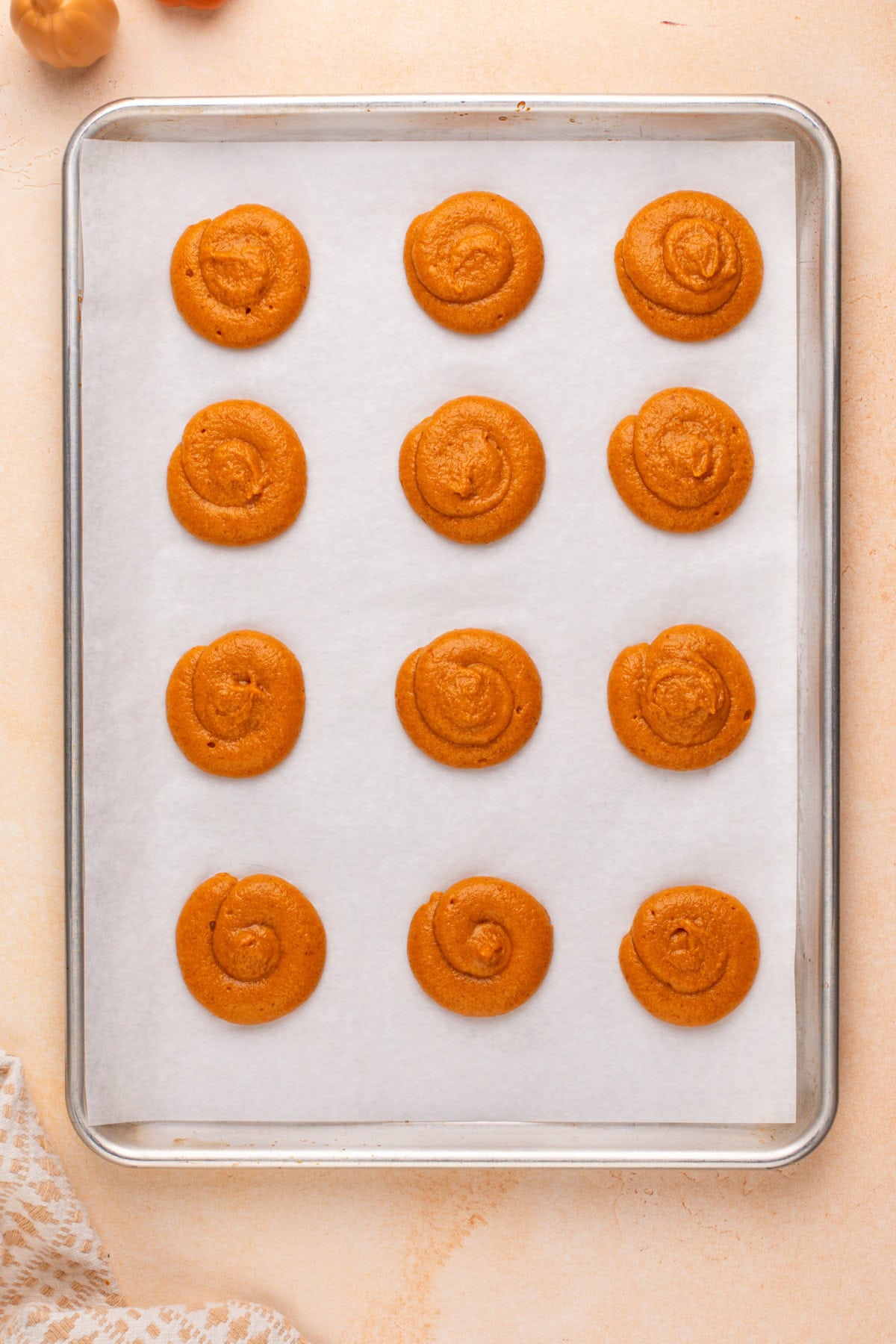 Pumpkin cookie batter piped onto a parchment-lined baking sheet, ready to go in the oven.