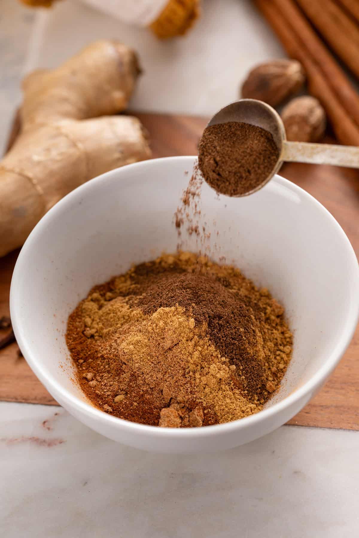 Spices for pumpkin pie spice being added to a small white bowl.