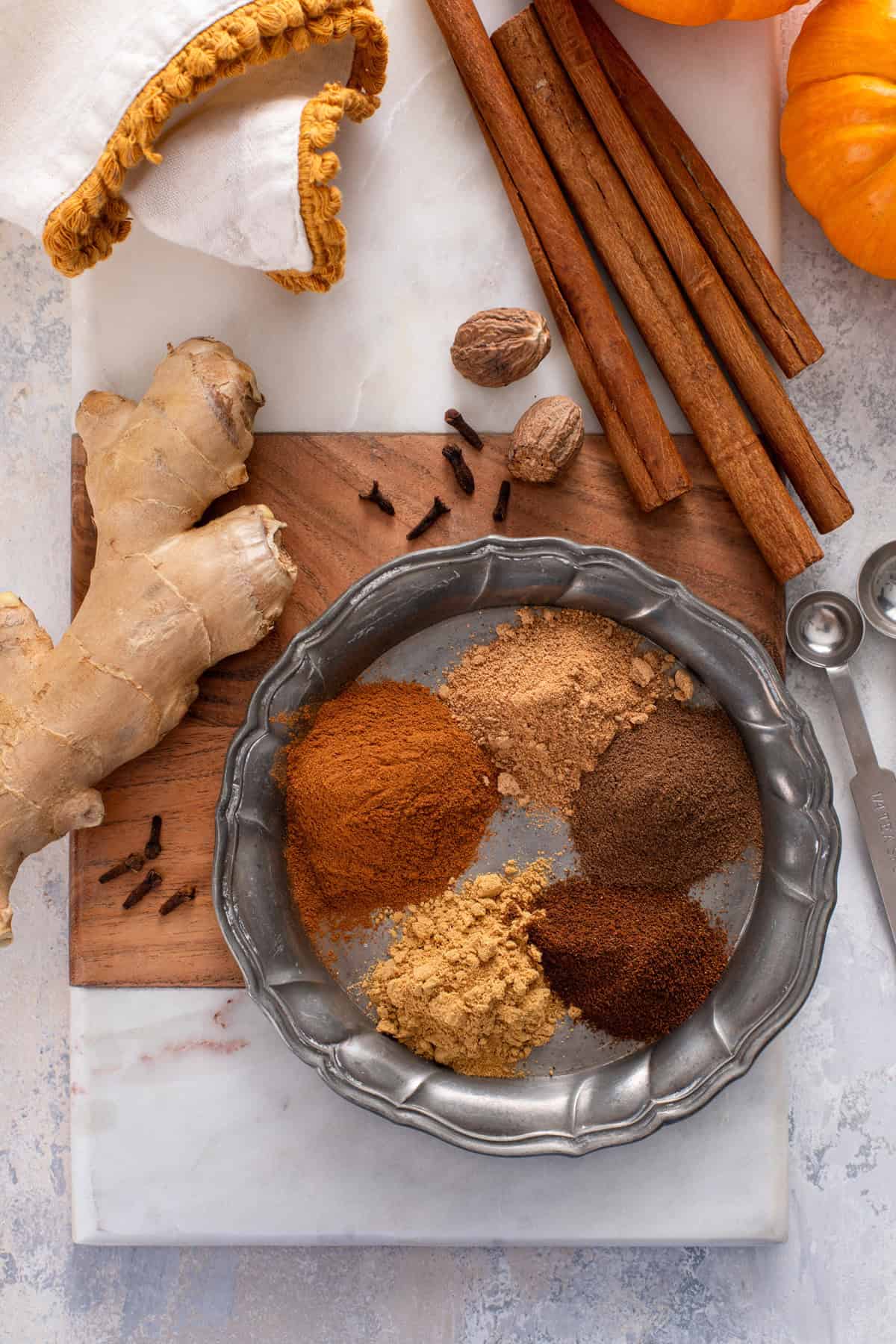 Individual spices for pumpkin pie spice measured out and arranged on a metal plate.