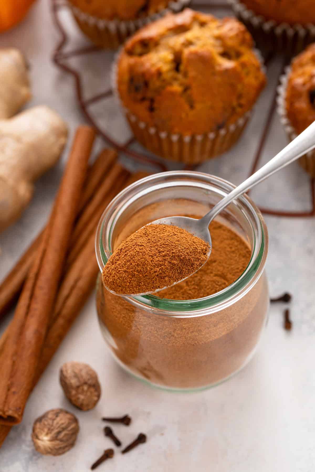 Jar of pumpkin pie spice with a spoonful of the spice balancing on the top.