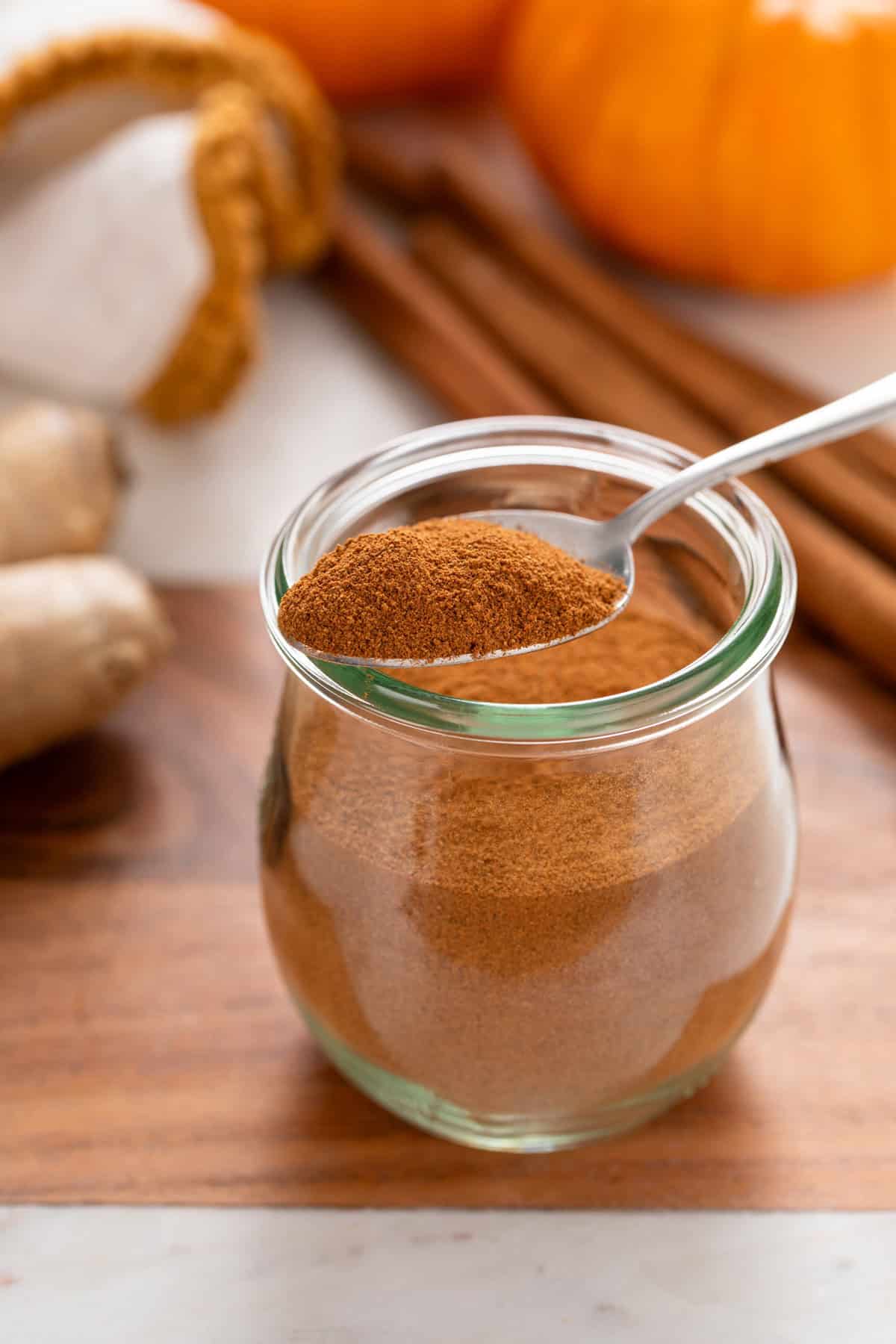 Jar of pumpkin pie spice with a spoonful of the spice resting on the lip.