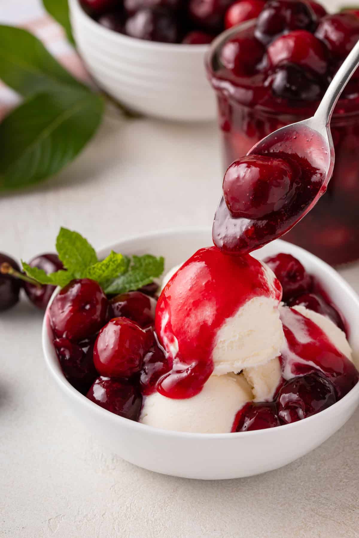 Cherry pie filling being spooned over vanilla ice cream.